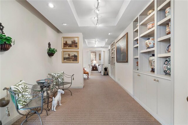 corridor featuring a tray ceiling, recessed lighting, rail lighting, light carpet, and baseboards