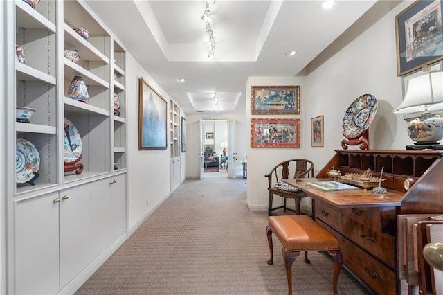 hallway with baseboards, a raised ceiling, track lighting, and light colored carpet