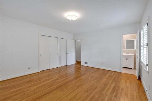 1618 Mason Mill Rd NE, Atlanta, GA 30329 - unfurnished bedroom featuring two closets, light wood-style floors, multiple windows, and ensuite bathroom