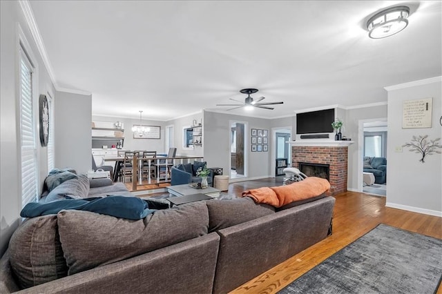 living room with ceiling fan, crown molding, wood-type flooring, and a fireplace