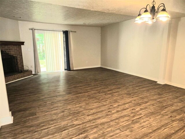unfurnished living room with a chandelier, dark wood finished floors, a brick fireplace, a textured ceiling, and baseboards