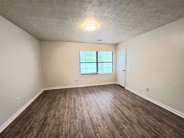 empty room with dark wood-type flooring, a textured ceiling, and baseboards