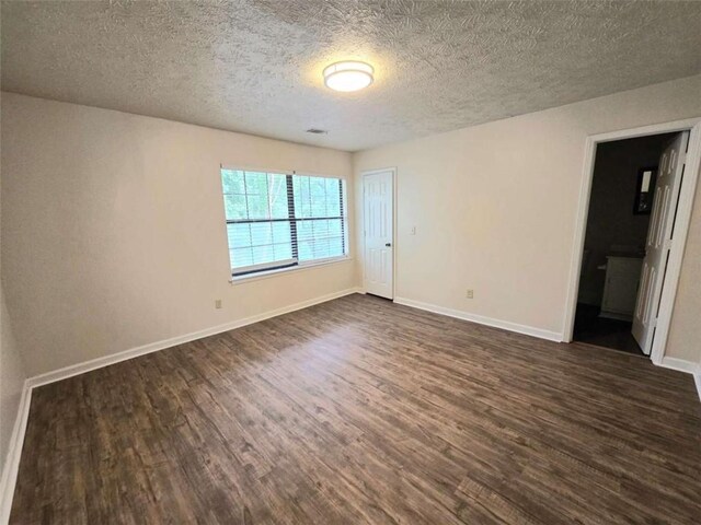 unfurnished bedroom with dark wood-style flooring, a textured ceiling, baseboards, and ensuite bath
