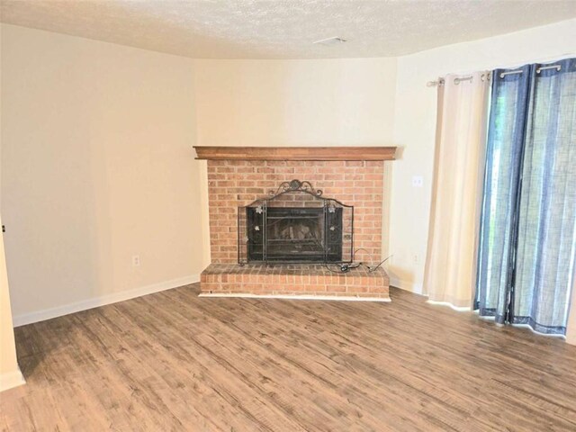unfurnished living room with wood finished floors, a brick fireplace, a textured ceiling, and baseboards