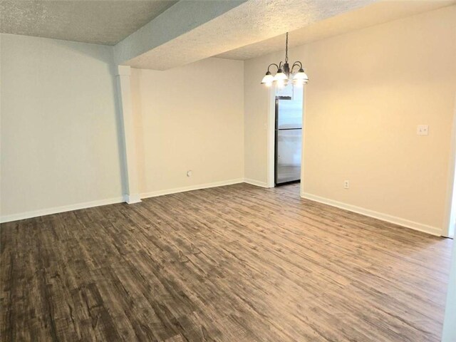 empty room with a chandelier, dark wood finished floors, baseboards, and a textured ceiling