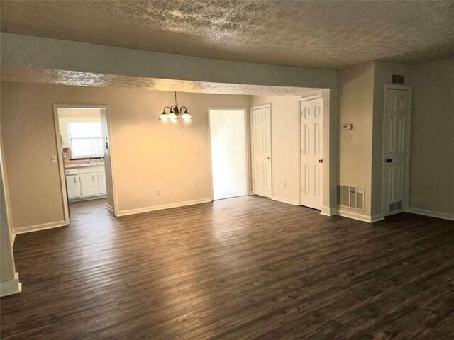 unfurnished living room featuring a chandelier, dark wood-type flooring, a textured ceiling, and baseboards