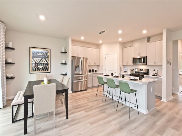 kitchen featuring a center island with sink, a breakfast bar, stainless steel appliances, light wood-type flooring, and recessed lighting