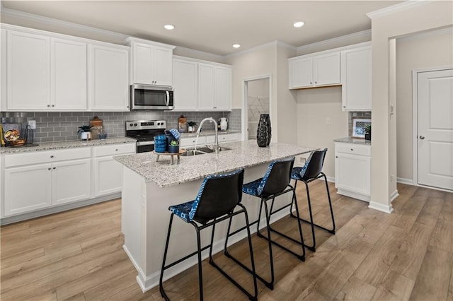 kitchen featuring a kitchen island with sink, stainless steel appliances, a sink, white cabinets, and light stone countertops