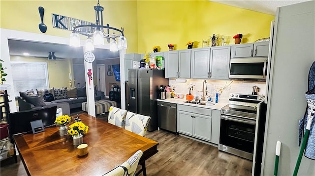 kitchen with appliances with stainless steel finishes, decorative backsplash, an inviting chandelier, dark wood-type flooring, and gray cabinets