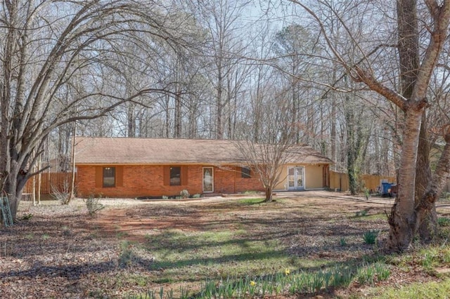 ranch-style home featuring dirt driveway, brick siding, and fence