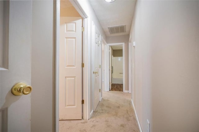 corridor with visible vents, light carpet, and baseboards