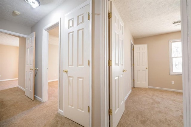 hall with light carpet, a textured ceiling, and baseboards