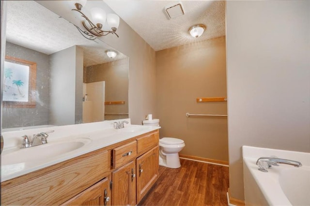 bathroom with toilet, wood finished floors, a garden tub, a textured ceiling, and a sink