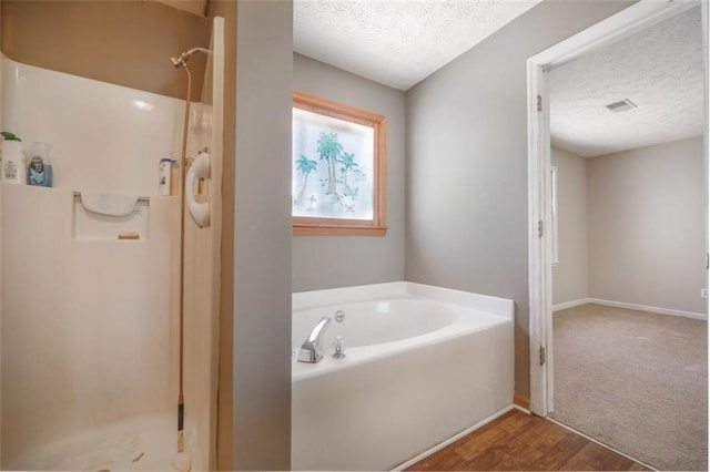 full bathroom featuring a stall shower, baseboards, visible vents, a garden tub, and a textured ceiling