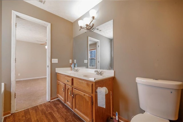 bathroom featuring double vanity, baseboards, toilet, wood finished floors, and a sink