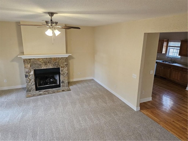 unfurnished living room with baseboards, a stone fireplace, a textured ceiling, and wood finished floors