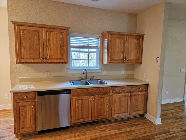 kitchen with brown cabinetry, dishwasher, light countertops, light wood-style floors, and a sink