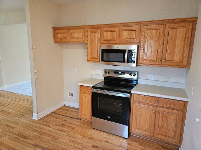 kitchen with stainless steel appliances, light wood finished floors, brown cabinetry, and light countertops