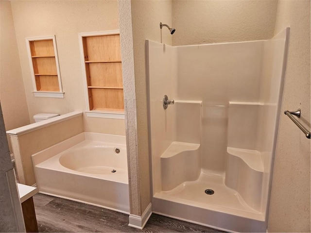 bathroom with a textured wall, a shower stall, a bath, and wood finished floors