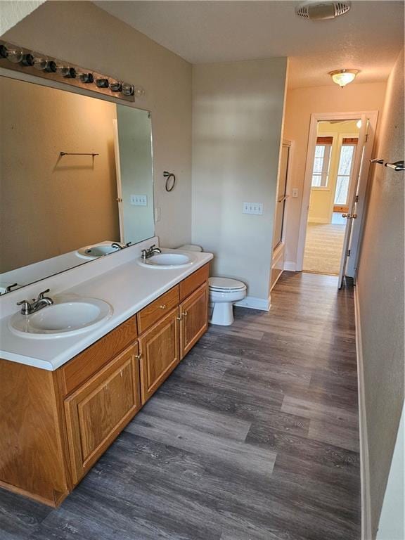 full bath featuring double vanity, wood finished floors, a sink, and toilet