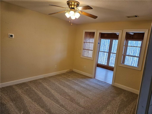 carpeted empty room with a textured ceiling, ceiling fan, visible vents, and baseboards