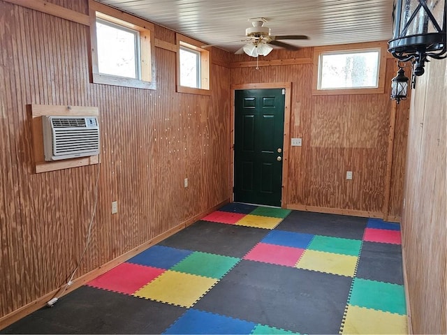 exercise room featuring ceiling fan, wooden walls, baseboards, a wall mounted AC, and tile patterned floors