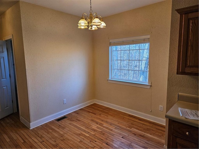 unfurnished dining area with baseboards, light wood finished floors, visible vents, and an inviting chandelier