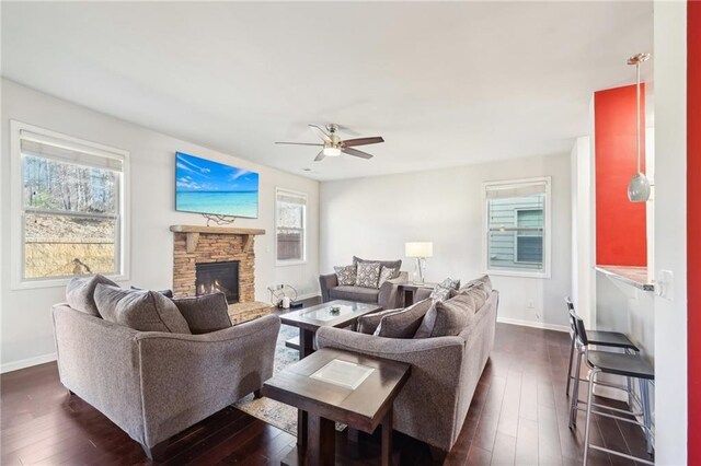 living room featuring ceiling fan, a healthy amount of sunlight, wood-type flooring, and a stone fireplace