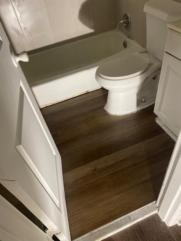 bathroom with a bath, vanity, toilet, and wood finished floors