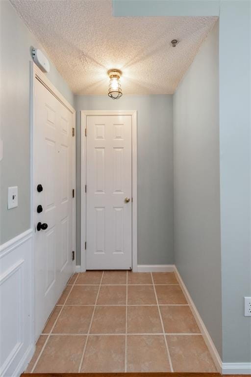 doorway featuring light tile patterned flooring, baseboards, and a textured ceiling