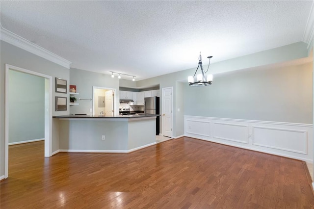 kitchen featuring a peninsula, under cabinet range hood, dark countertops, a notable chandelier, and open floor plan