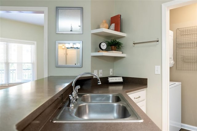 kitchen with open shelves, washer / clothes dryer, a sink, white cabinets, and dark countertops