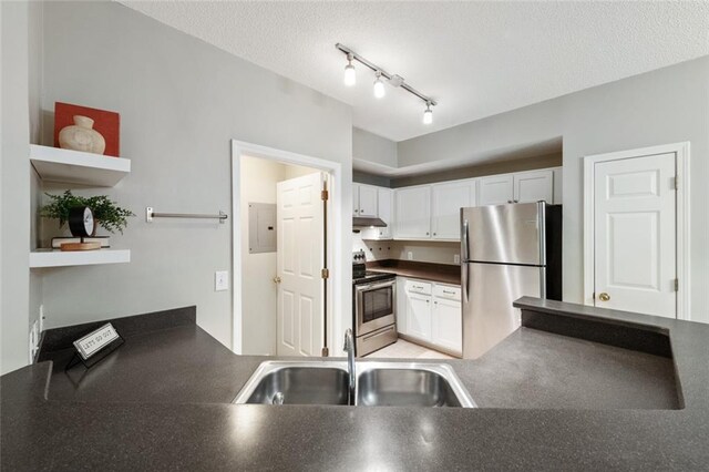 kitchen with a sink, under cabinet range hood, dark countertops, white cabinetry, and appliances with stainless steel finishes