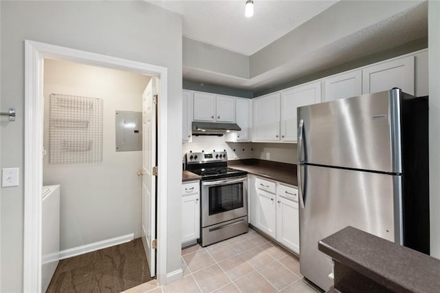 kitchen featuring dark countertops, under cabinet range hood, electric panel, appliances with stainless steel finishes, and white cabinets