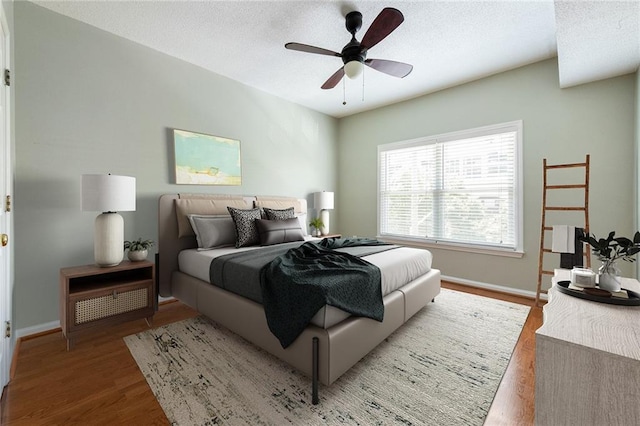 bedroom with a ceiling fan, wood finished floors, baseboards, and a textured ceiling