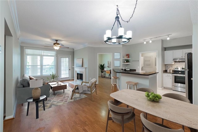 dining room featuring baseboards, light wood-type flooring, ornamental molding, ceiling fan with notable chandelier, and a fireplace