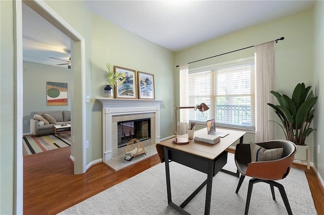 office featuring baseboards, a textured ceiling, wood finished floors, and a fireplace