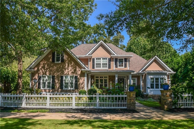 craftsman house with a fenced front yard and a shingled roof