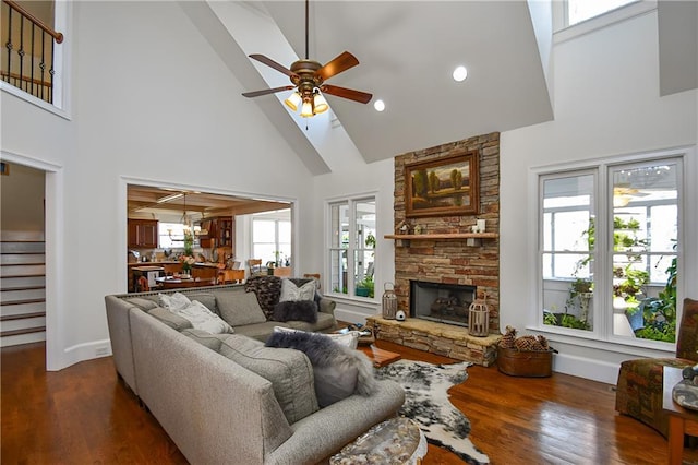 living area featuring a fireplace, a ceiling fan, dark wood-type flooring, and stairs