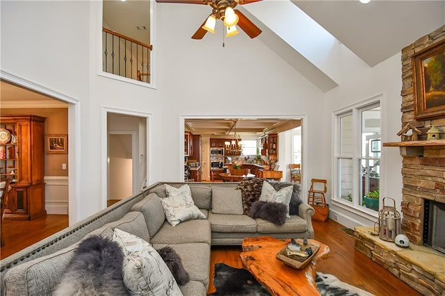 living area featuring ceiling fan with notable chandelier, high vaulted ceiling, wood finished floors, and a fireplace