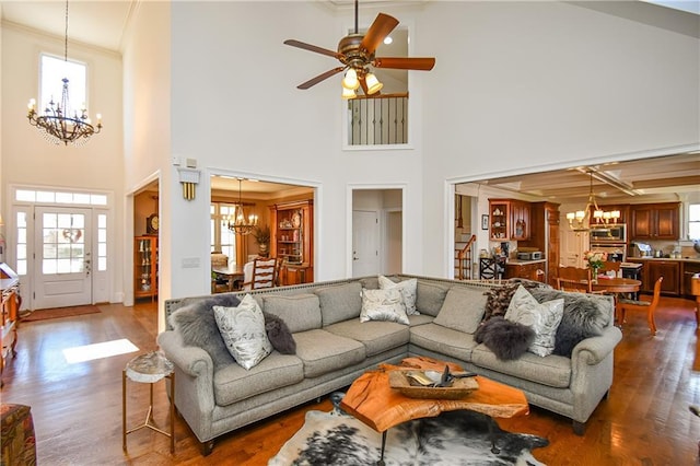 living area featuring stairway, ornamental molding, dark wood-type flooring, and ceiling fan with notable chandelier