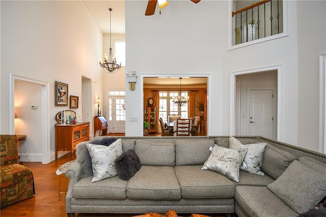 living room with a towering ceiling, ceiling fan with notable chandelier, ornamental molding, baseboards, and wood finished floors