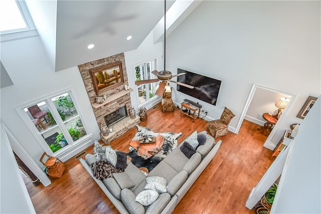 living room featuring light wood-type flooring, a high ceiling, a stone fireplace, and a ceiling fan