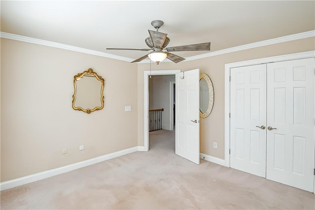 unfurnished bedroom featuring a closet, light colored carpet, ornamental molding, ceiling fan, and baseboards