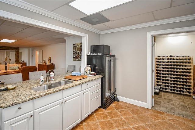 kitchen with white cabinetry, crown molding, light stone counters, and a sink