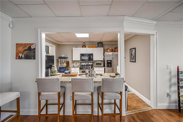 kitchen featuring white cabinets, light stone counters, a breakfast bar, stainless steel appliances, and a sink