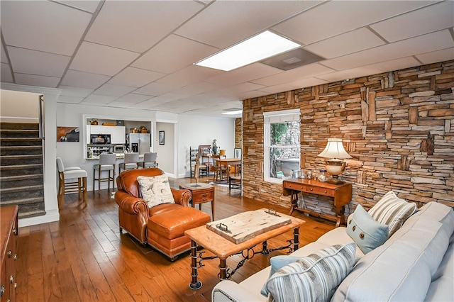 living area with wood finished floors, a drop ceiling, and stairs