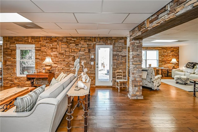 living area featuring wood finished floors, a healthy amount of sunlight, decorative columns, and a drop ceiling