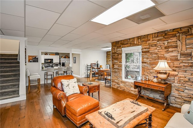 living room with a paneled ceiling, stairs, and wood finished floors