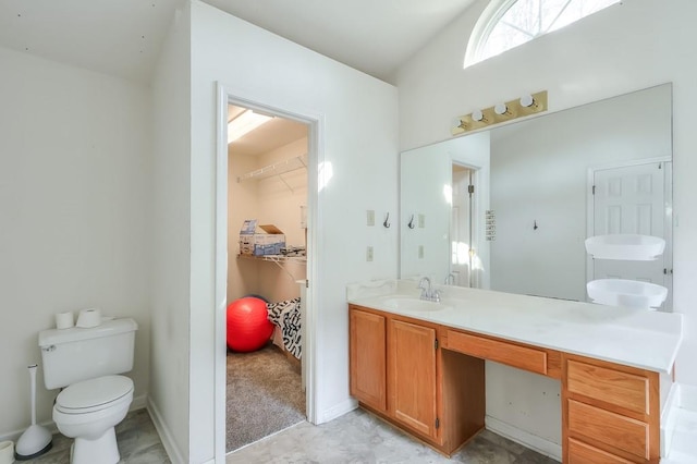 bathroom with a walk in closet, baseboards, toilet, and vanity